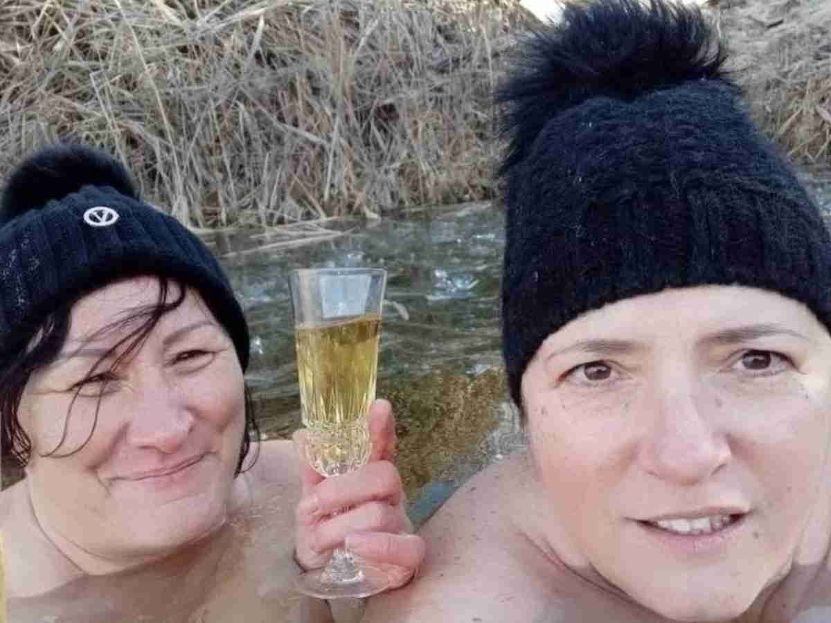 Két barátnő pezsgőspohárral koccint a jeges tóban szilveszter napján.